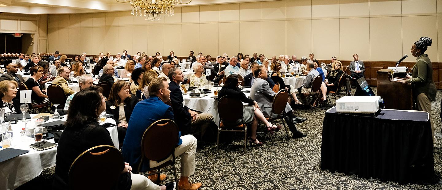 woman speaking at a podium to a room full of people