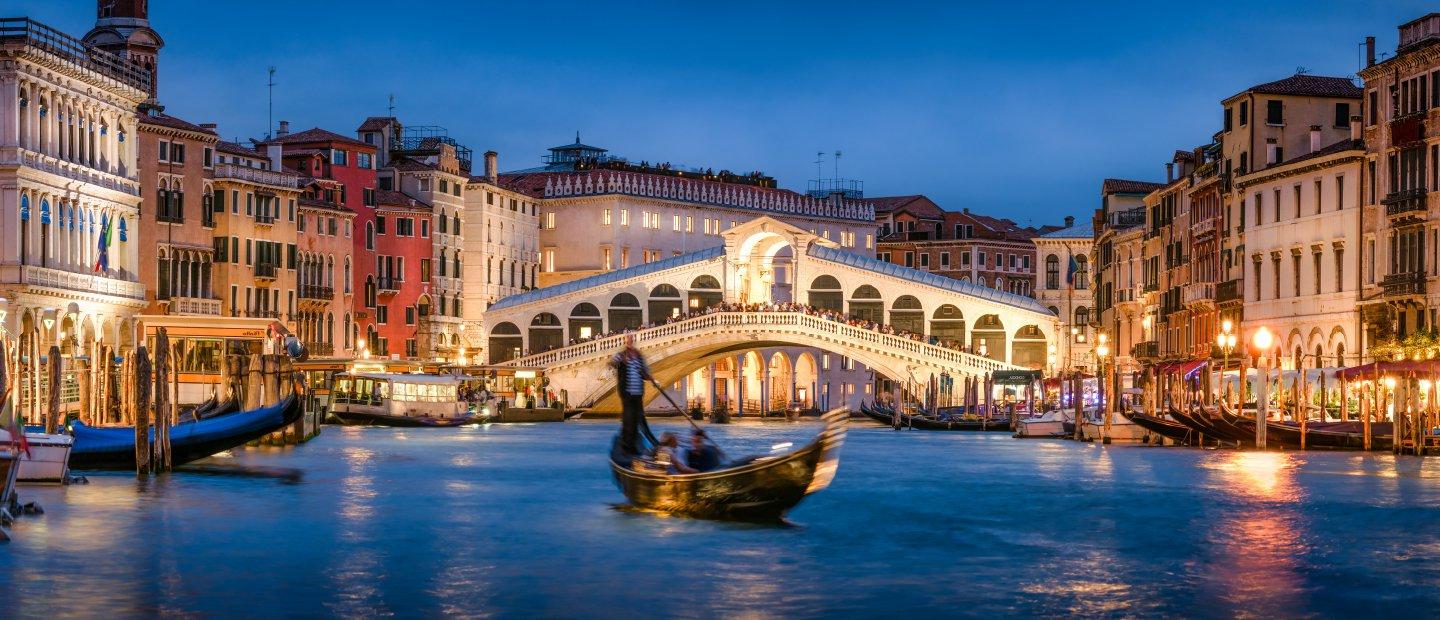 People on a gondola in a canal at night in Italy.