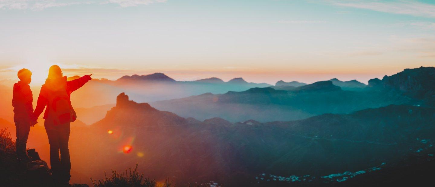 Two people standing on a peak overlooking mountains.